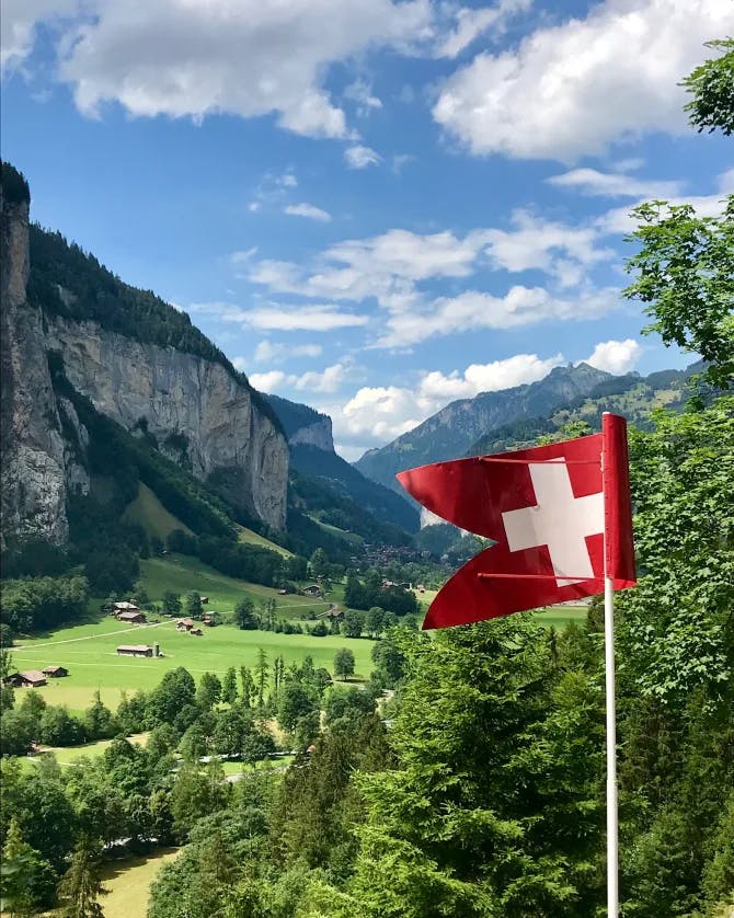 Switzerland flag with a beautiful view of foliage and mountain scapes in the country. 