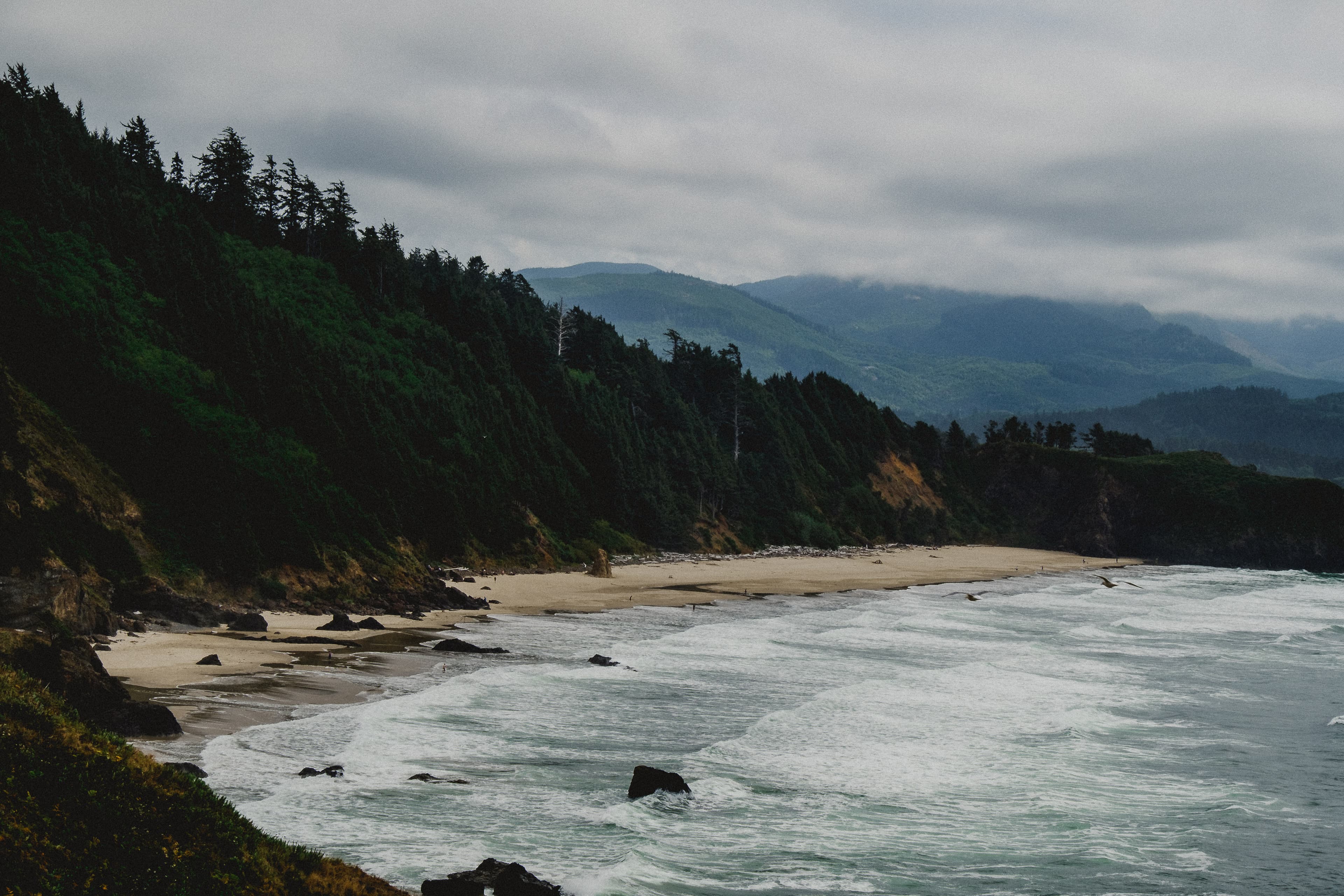 View of the coastline on an overcast day, with a view of green mountains and sky.