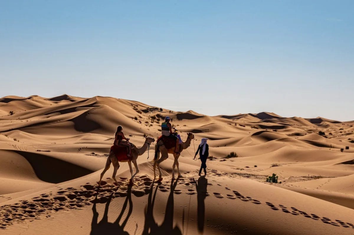 Two travelers are guided by a local as they venture through the dunes of the Sahara