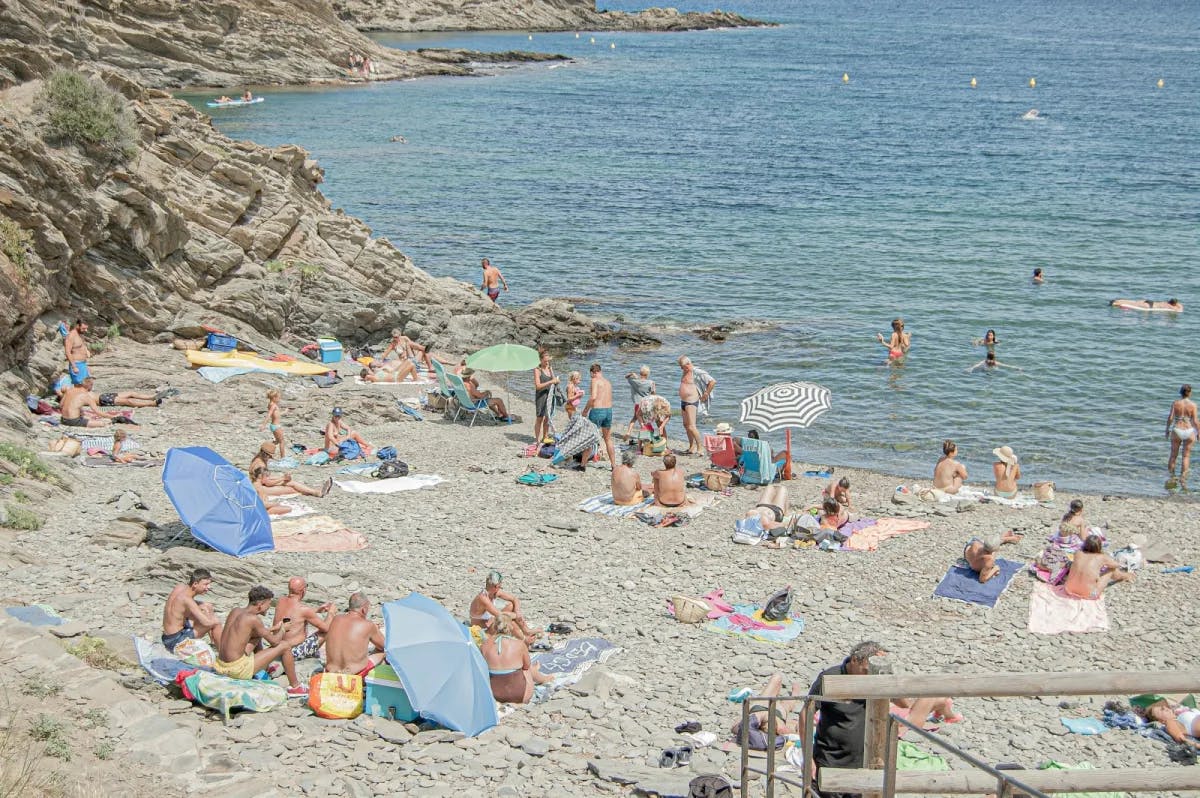 Dozens of travelers relax on a beach in Cadaqués, Spain 