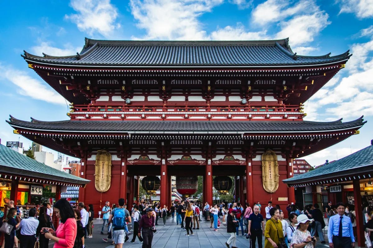 Elaborate historical architecture in Asakusa, Tokyo. Hundreds of visitors peruse the grounds of the historical site as the old tower prominently stands over them