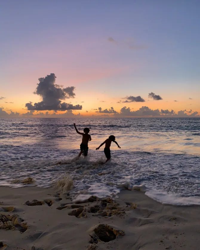 Two kids playing in the sea at sunset