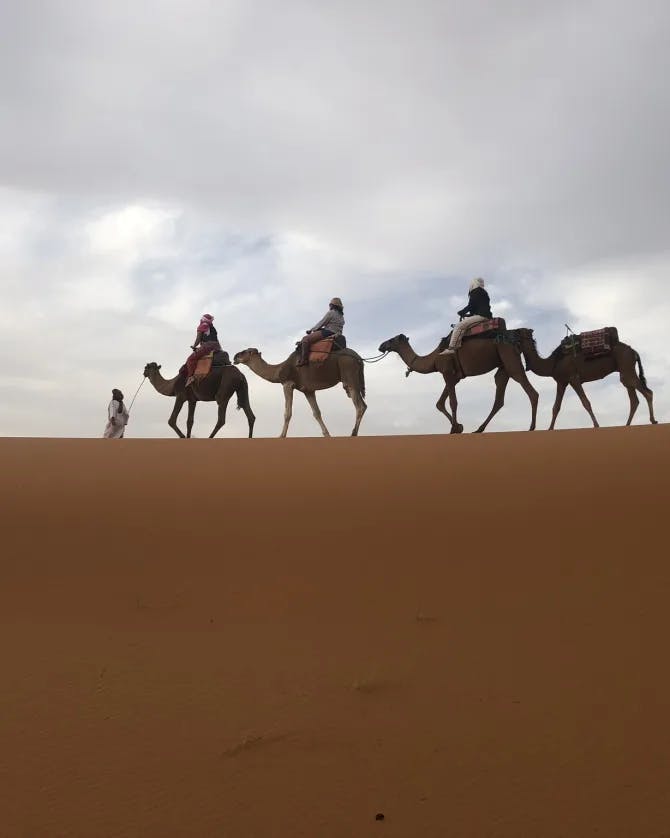 People riding camels in the desert with a cloudy sky