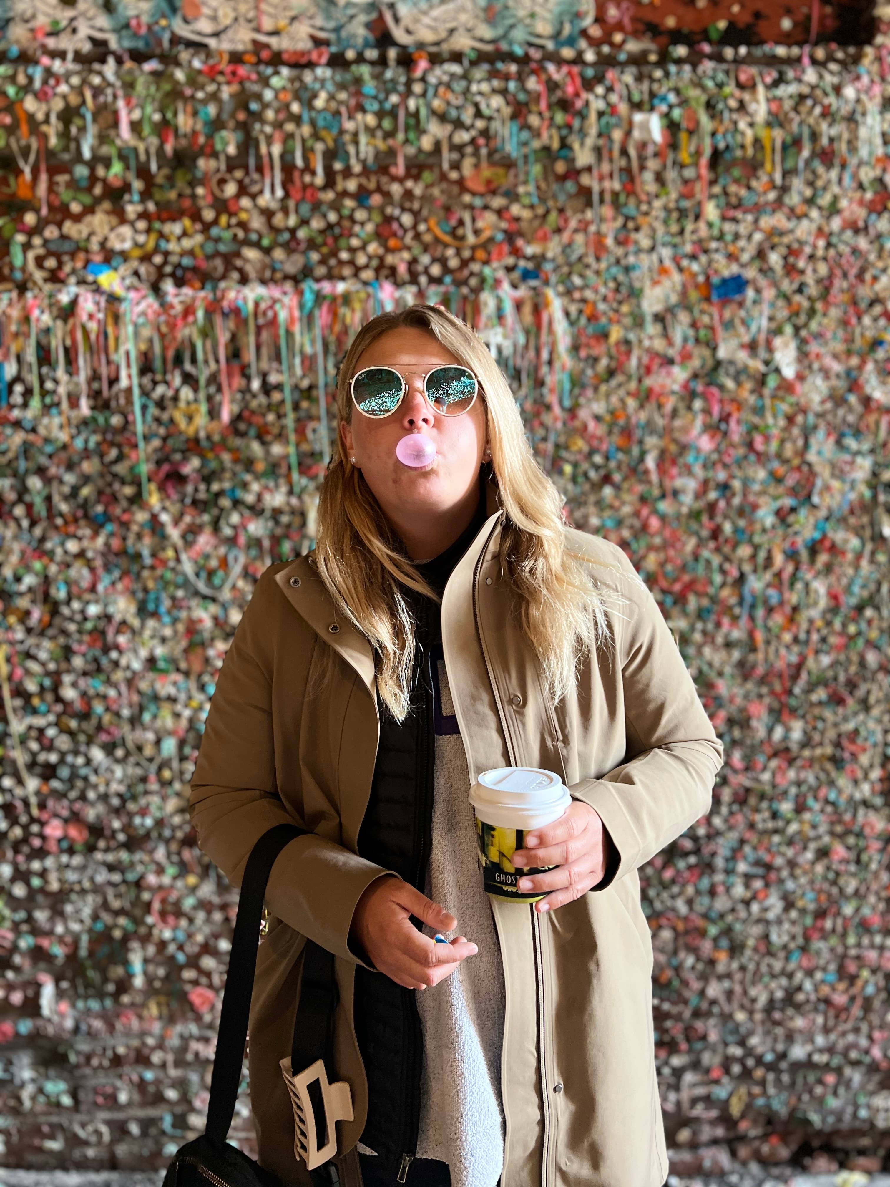 bubble gum wall with Brittany blowing a bubble with a coffee in hand.