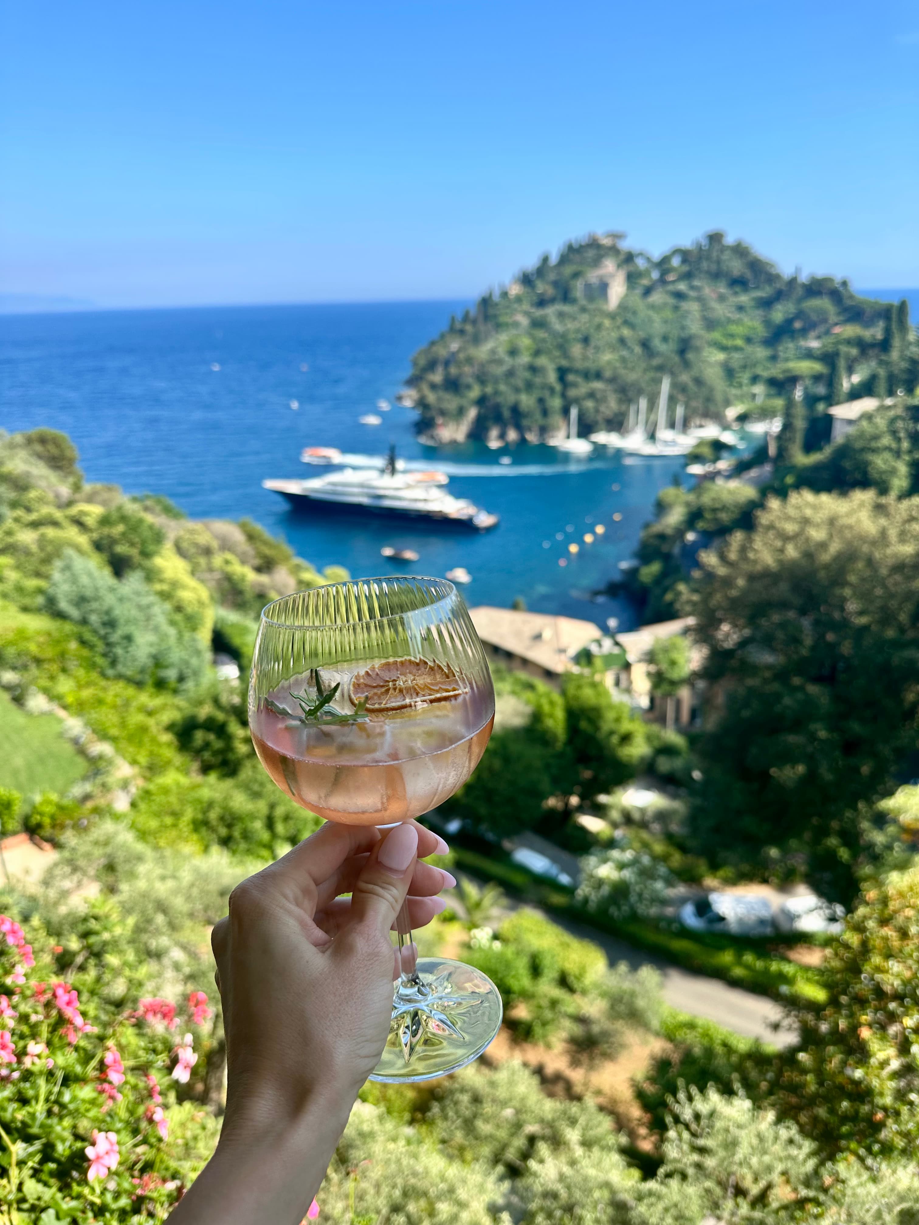 Picture of glass filled with juice in hand in front of an aerial view of trees and a boat sailing out to sea
