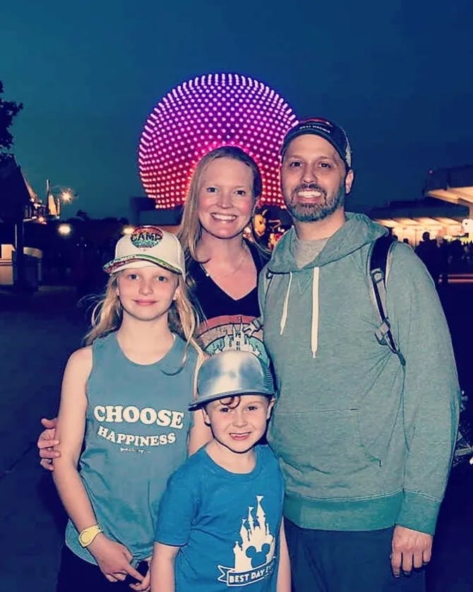 A family posing for a photo at an amusement park with a round pink light feature in the background