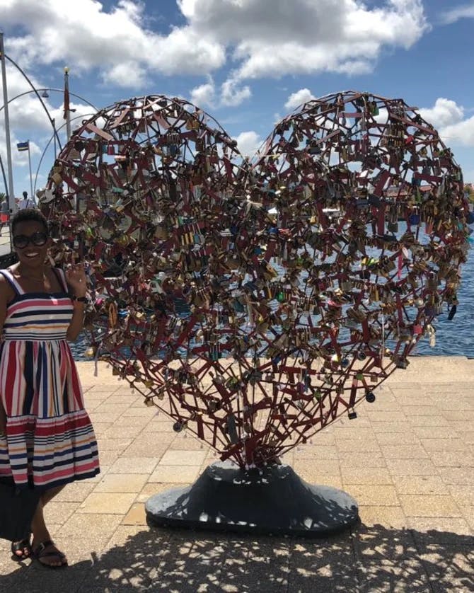 Kenya wearing a striped dress and posing next to a heart statue outside in front of a body of water