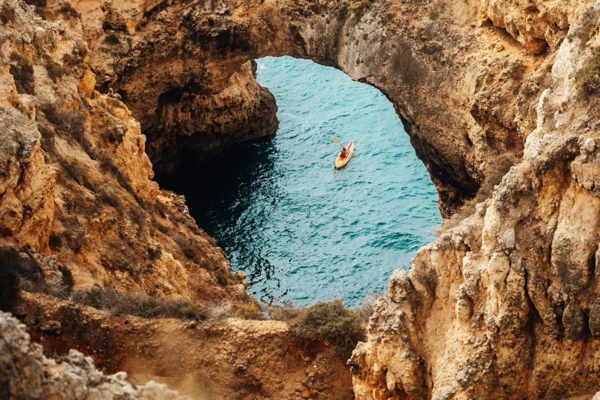 A view through a bizarre rock formation: a lone kayaker paddles off the shores of Lagos, Portugal