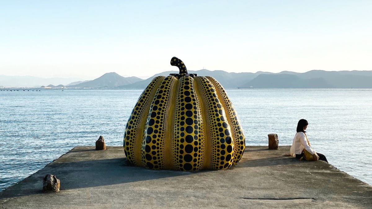 Brown and white pumpkin statue on the edge of a boardwalk on the water. 