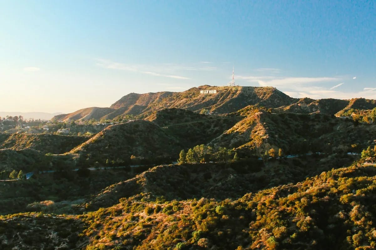 Golden, rugged hills lead up to a large outcropping in the distance where the Hollywood sign is faintly visible