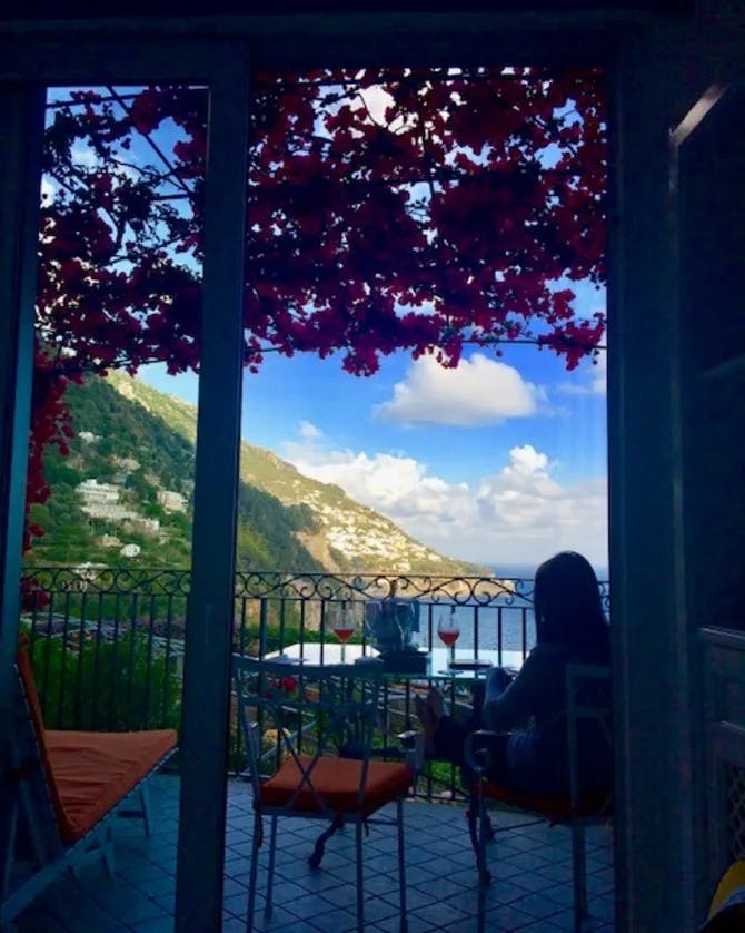 Picture of Cassie's silhouette at a table looking out at a view of the sea and a mountain range with flowers hanging above her