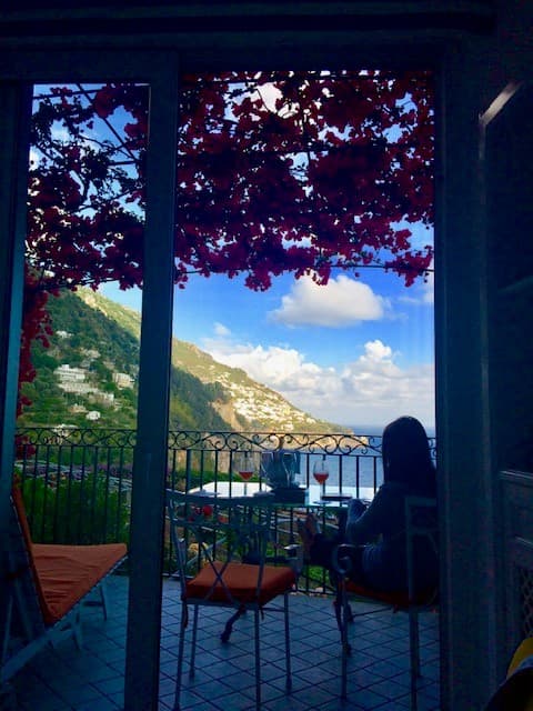 Picture of Cassie's silhouette at a table looking out at a view of the sea and a mountain range with flowers hanging above her