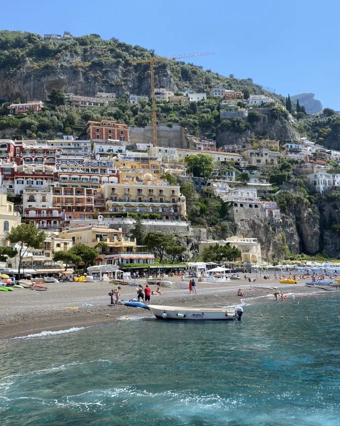 A view of the beach and Amalfi coast in Italy with people and boats placed throughout the scenery
