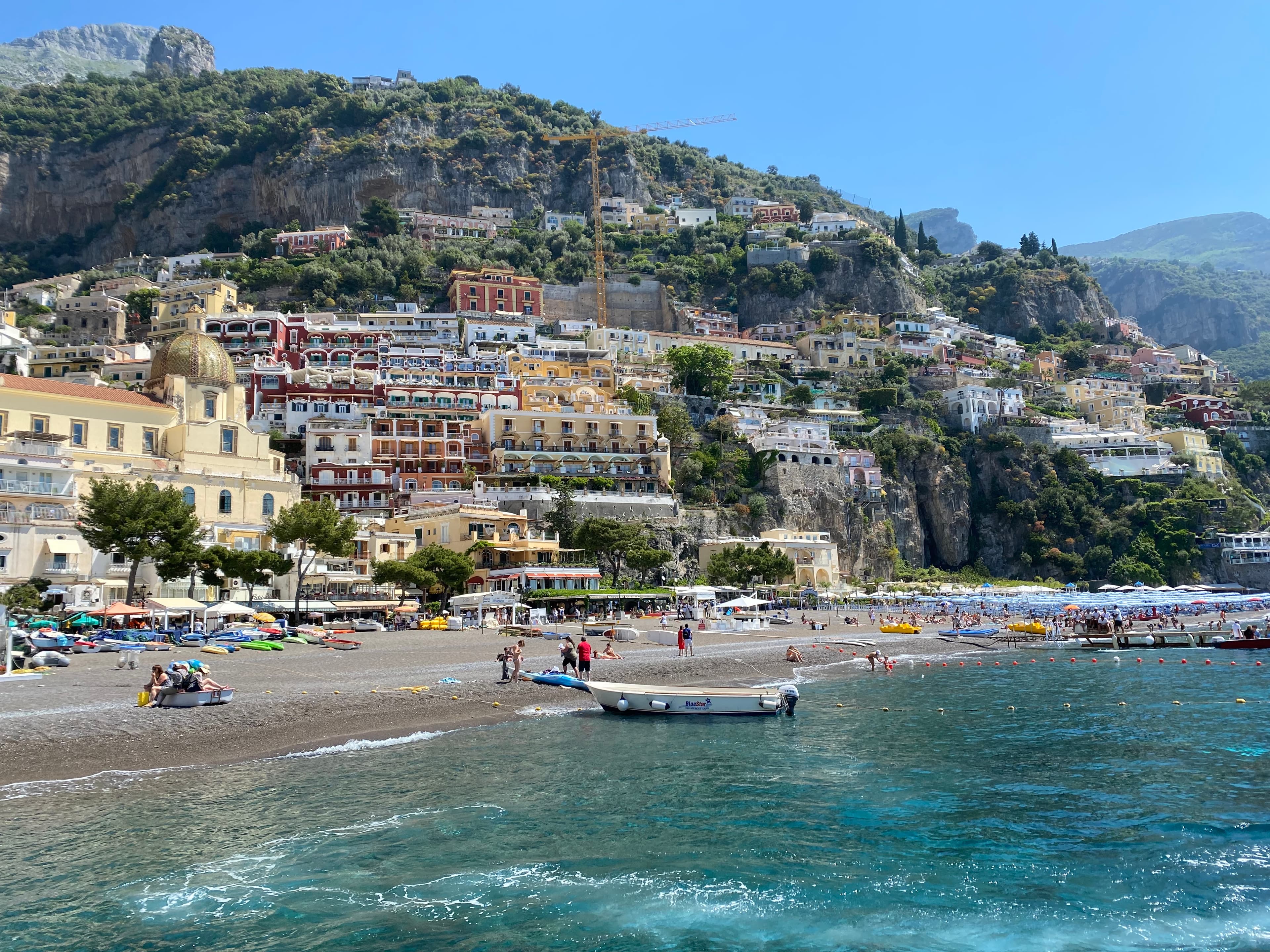 A view of the beach and Amalfi coast in Italy with people and boats placed throughout the scenery