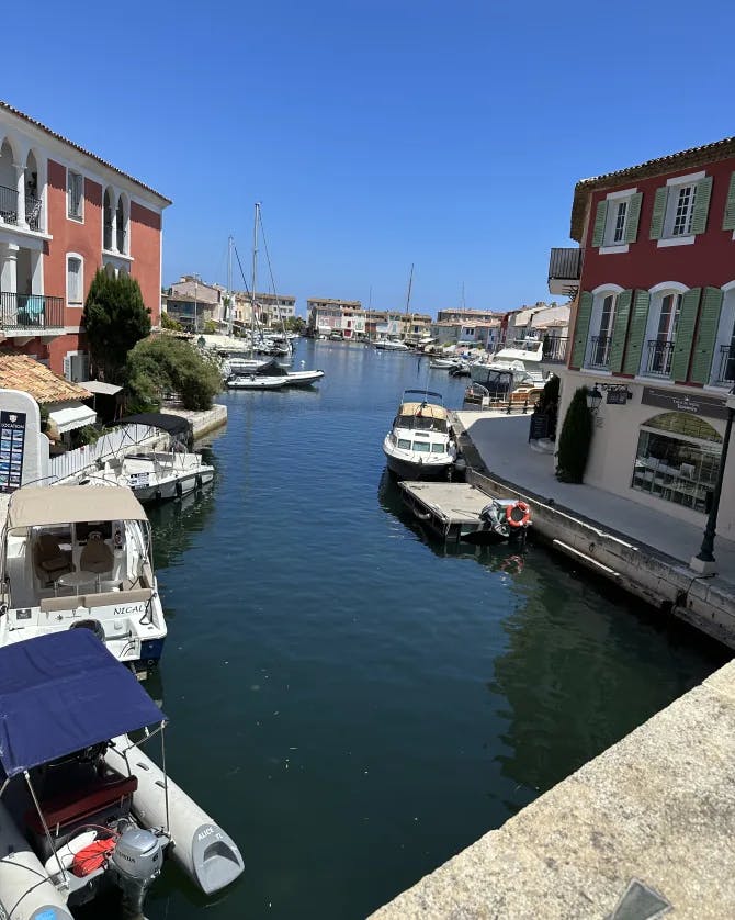 Picture of Port Grimaud featuring a water canal and two red-toned buildings on each side surrounded by docked boats 