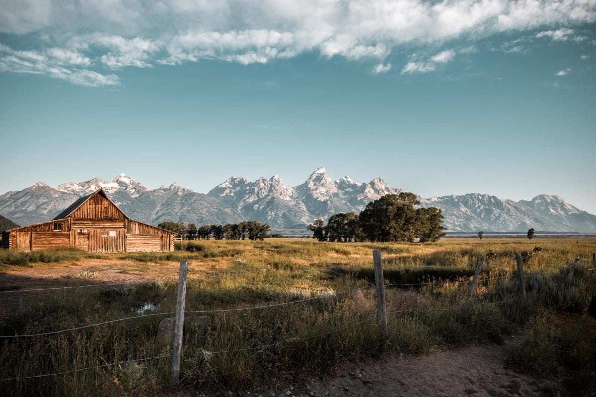 old barn in a grassy field with views of the Tetons