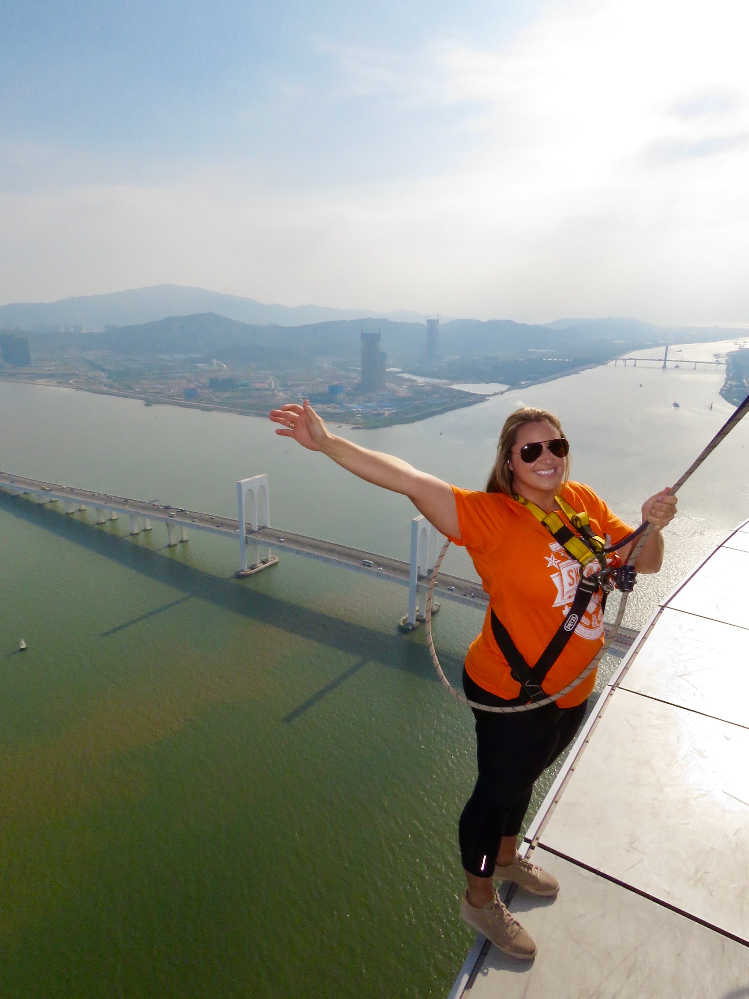 A picture of Ashley wearing an orange top and black pants preparing to bungee jump at Macau Tower Convention and Entertainment Center