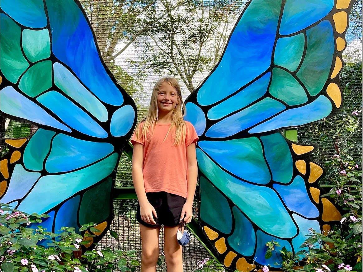 A girl standing in front of a blue and yellow butterfly statue.