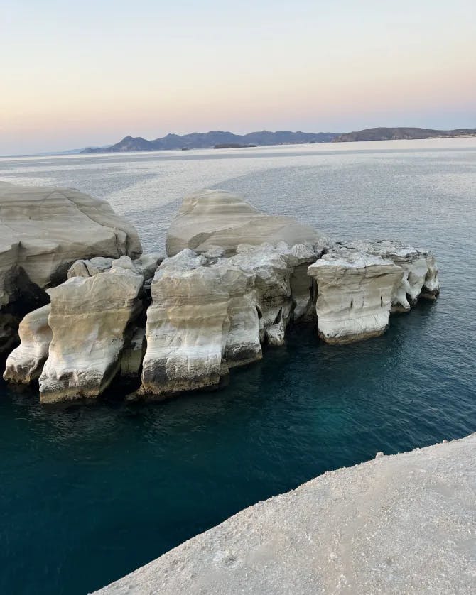An aerial view of Sarakiniko Beach surrounded by water and a sunset