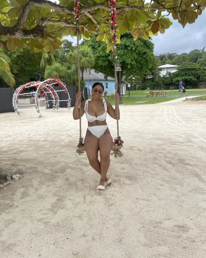 Tyler wearing a white bathing suit on a wooden swing over the beach with trees in the background.