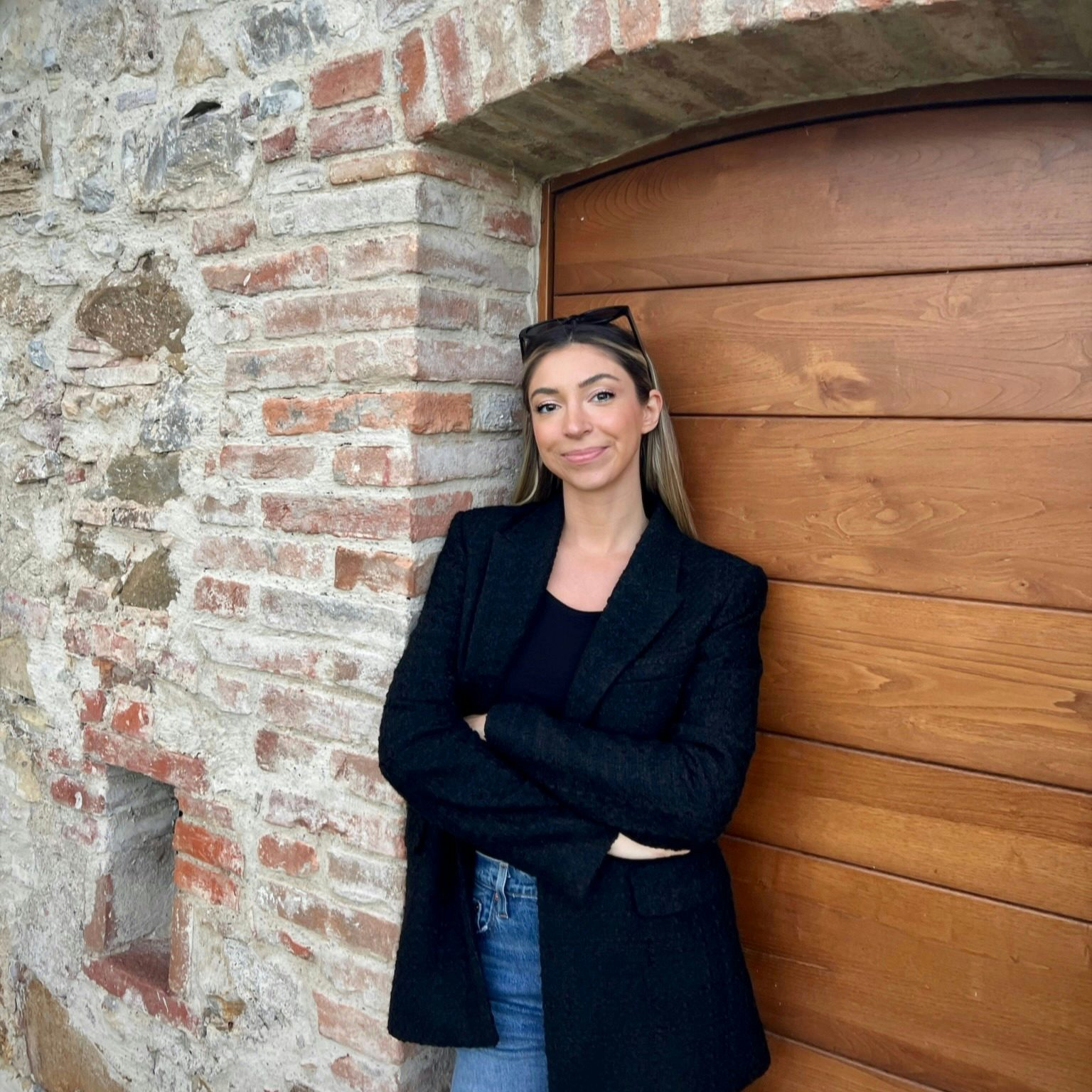 Travel Advisor Emily Herlan with a black jacket, standing in front of a wooden door and brick building.