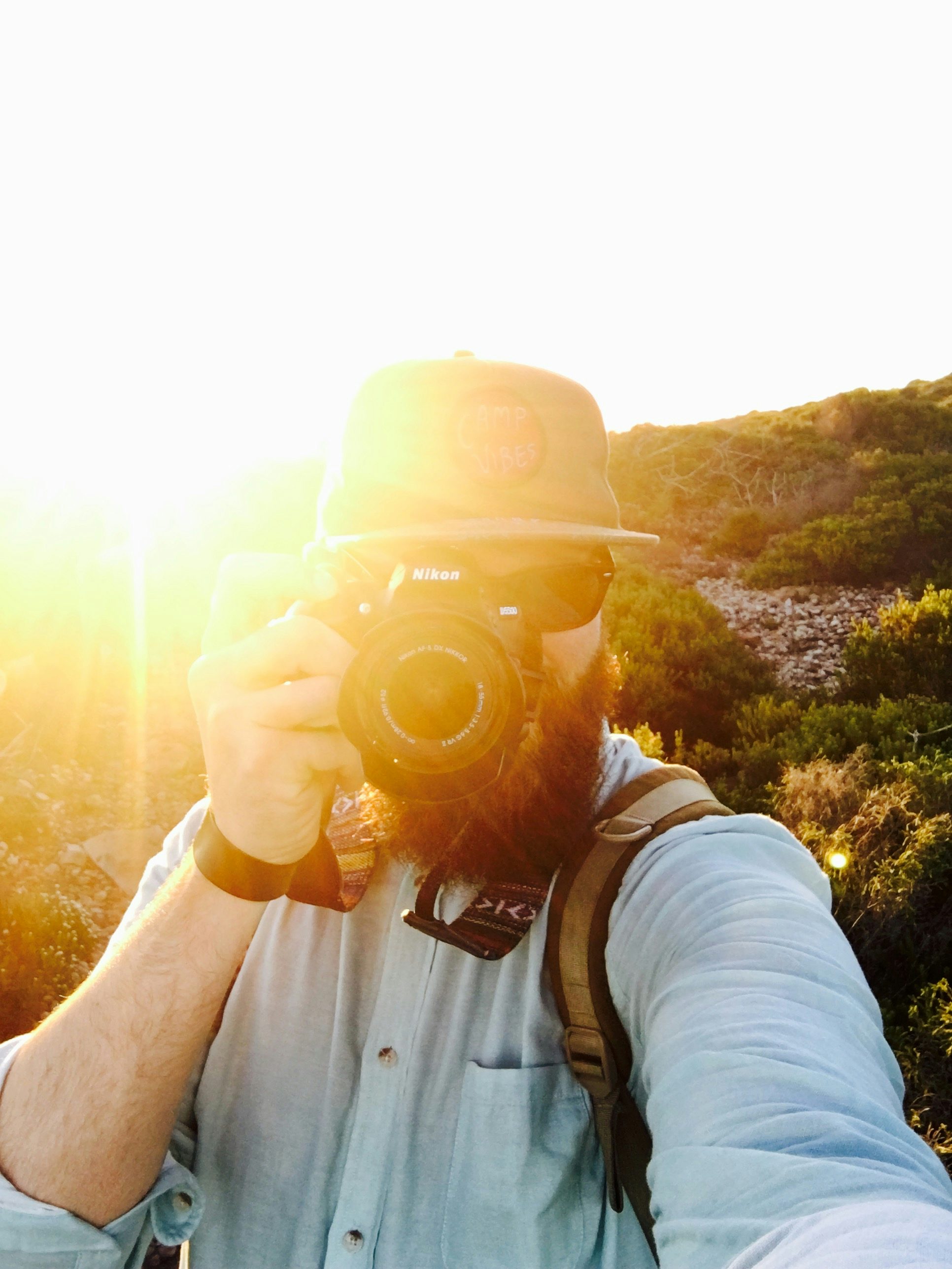 Travel Advisor Jeff Karges holds a camera up to his eye with the sun peaking out behind his shoulder wearing a straw hat 