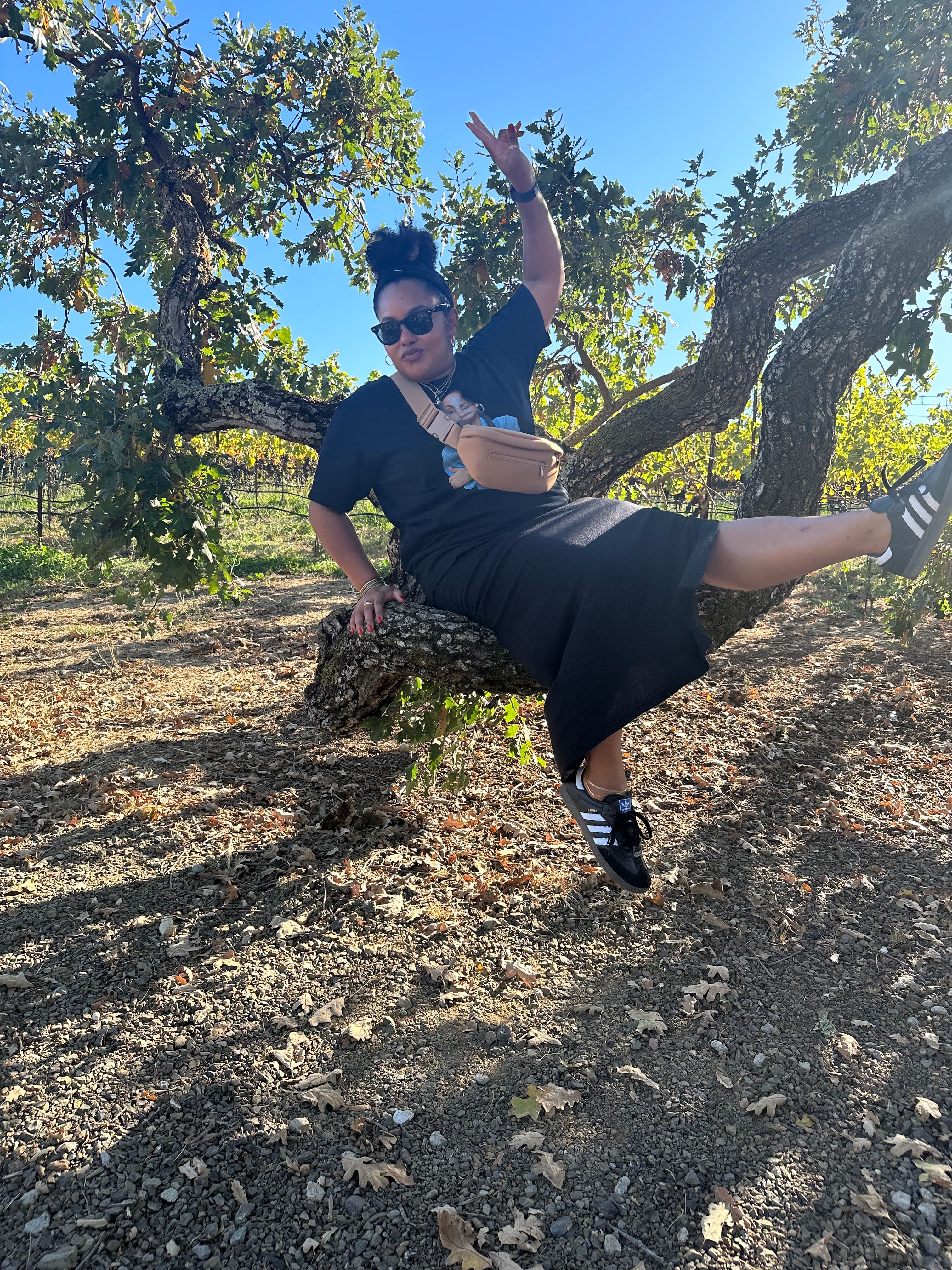 Shannon outside on a sunny day posing on a curved tree branch.