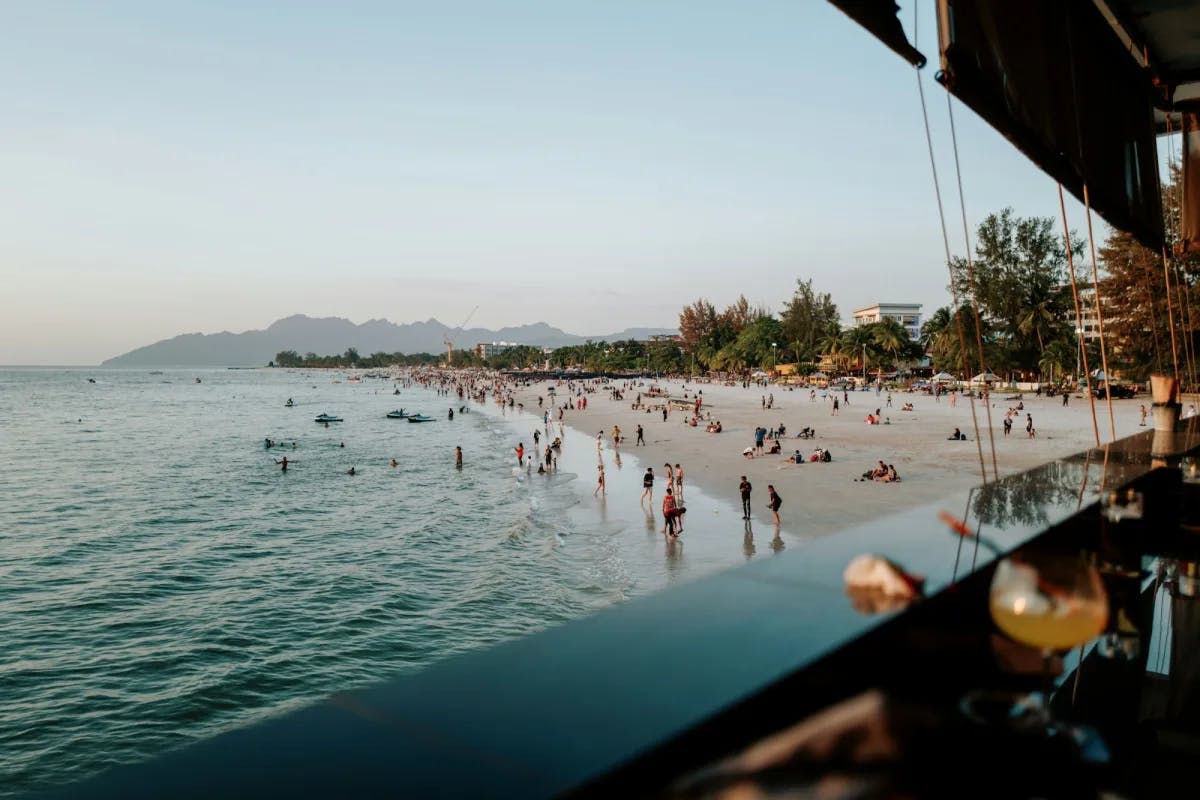 A view from a pier-bound cocktail lounge: hundreds of beachgoers enjoy the calm waters of Langkawi, Kedah, Malaysia