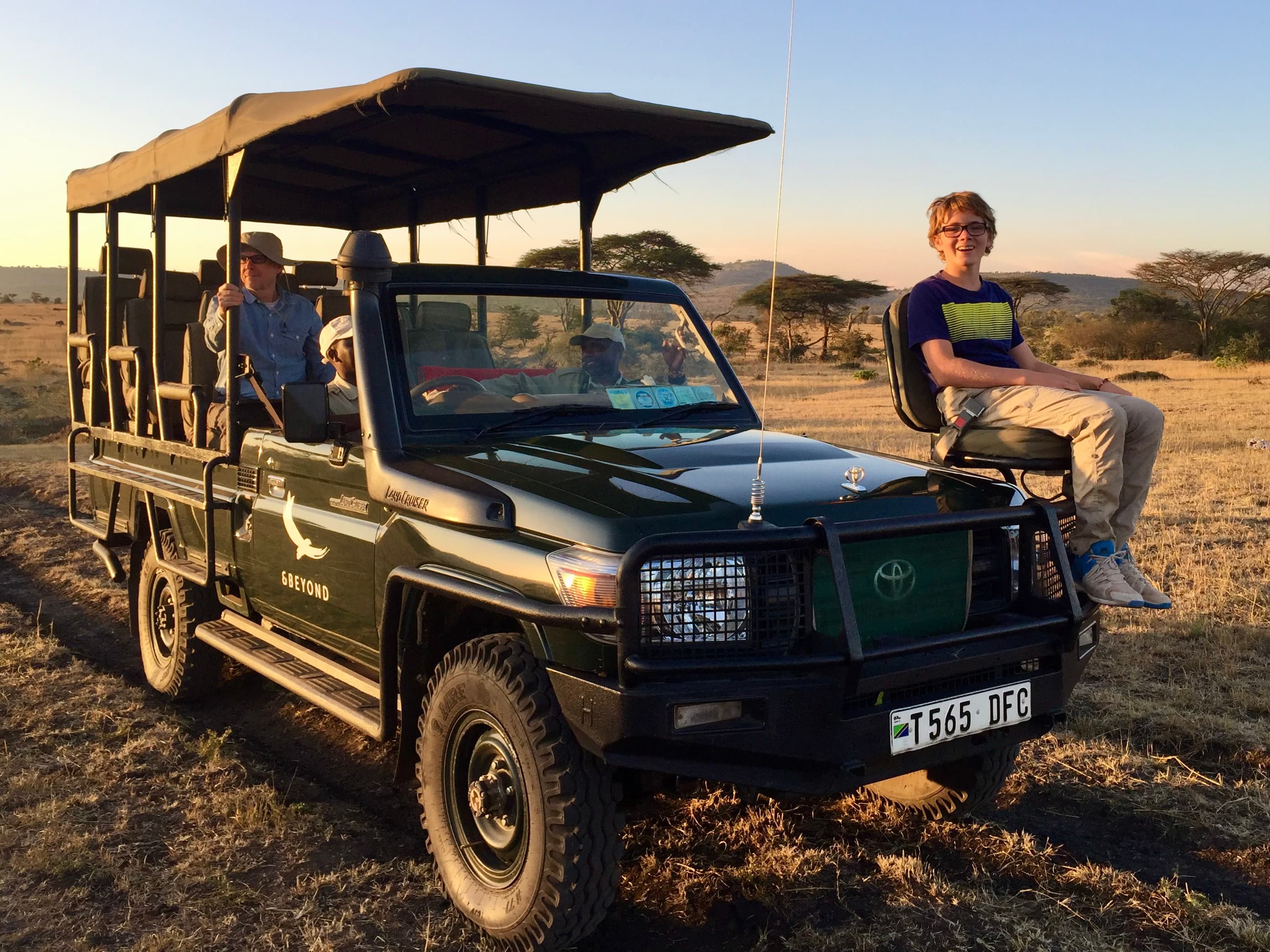 A person sitting on the front of a safari truck outside at sunset