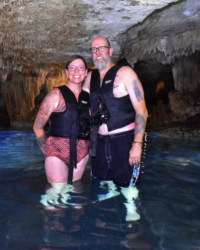 Susan wearing a swimsuit and standing next to her partner in a cave with water