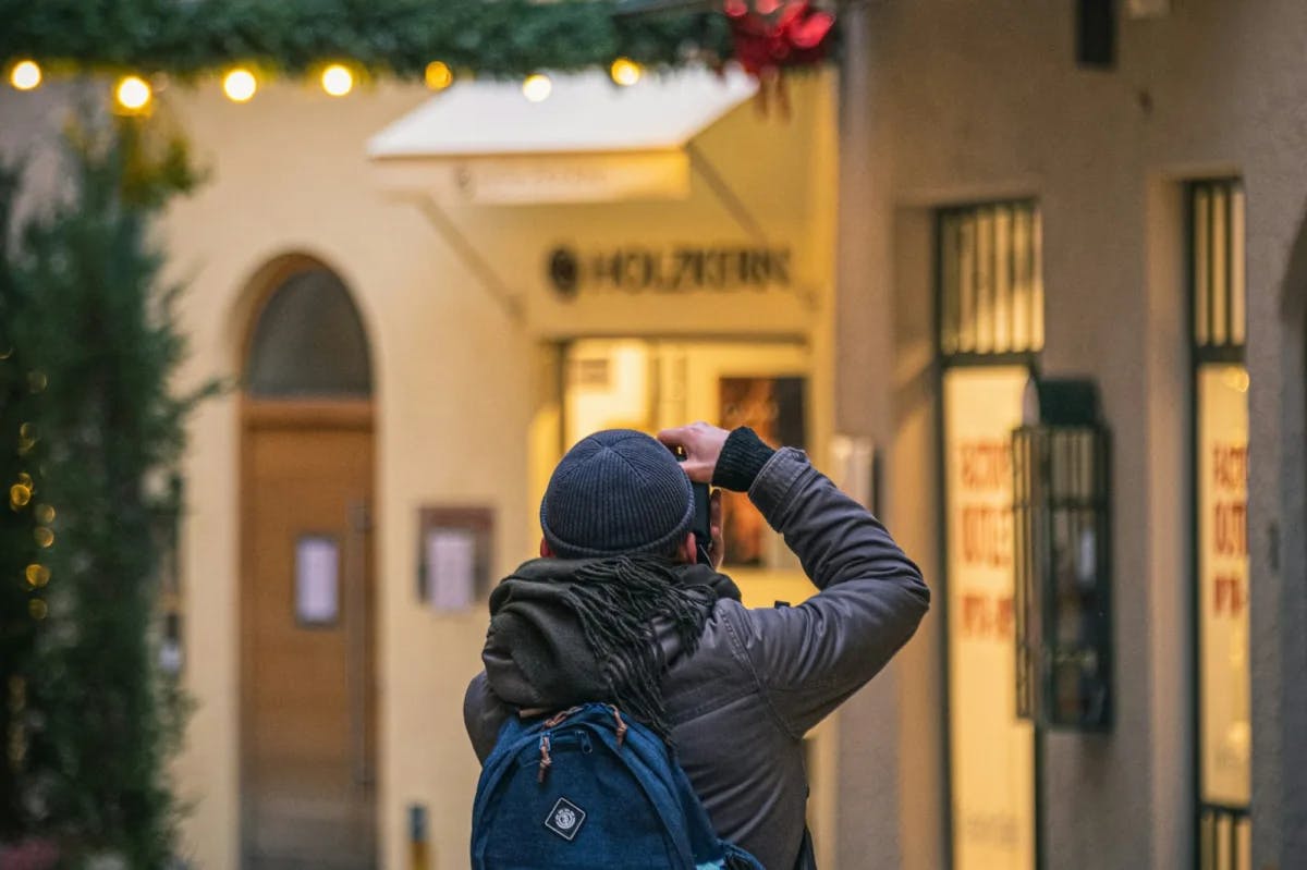 A man in trendy clothing takes photos with his phone of a Christmas market in Salzburg