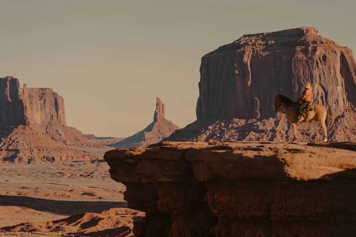 A traveler on horseback looks out over the empty expanse of Monument Valley as dust clouds obscure the far distance