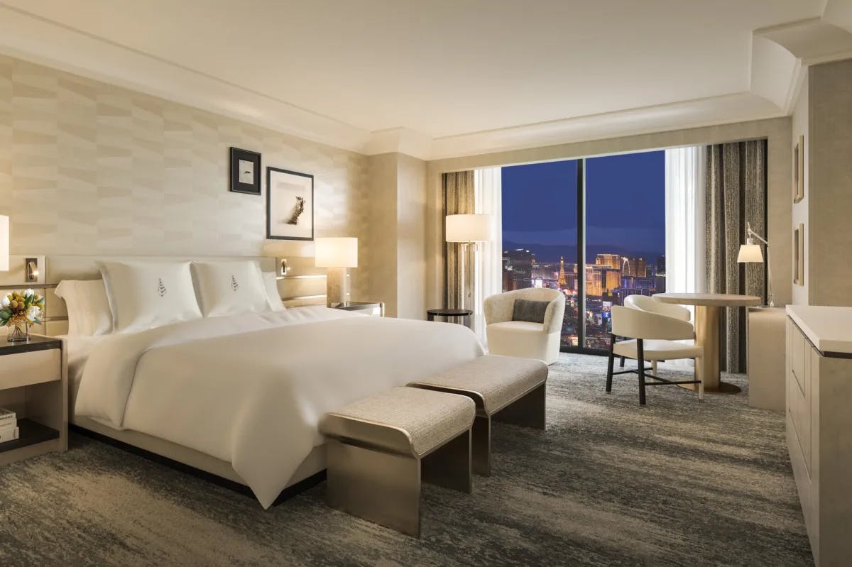 Plush, elegant furnishings fill a spacious guest room at Four Seasons Hotel Las Vegas while the floor-to-ceiling windows reveal the Vegas Strip