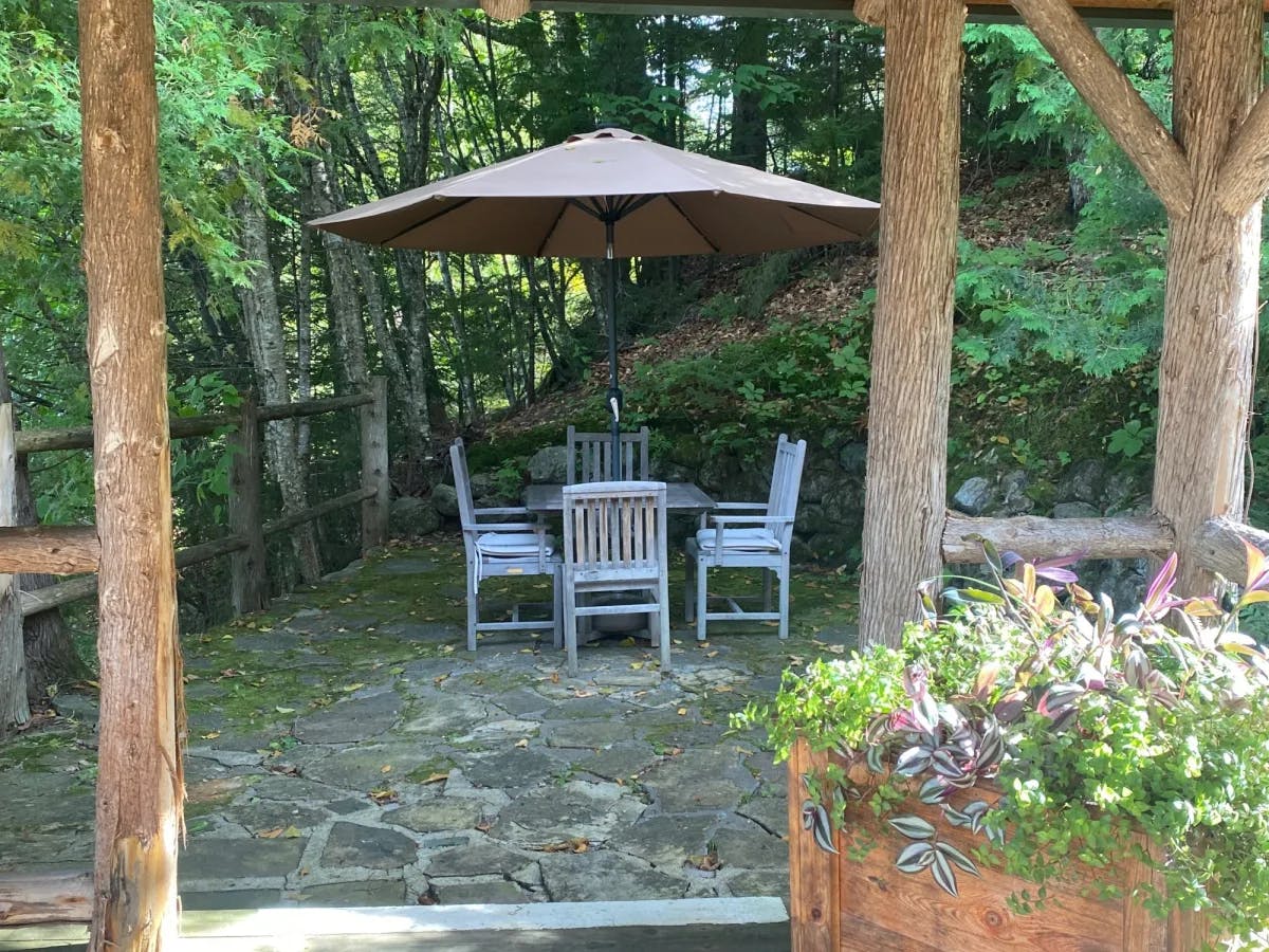 An outdoor sitting area under an umbrella with four chairs.  
