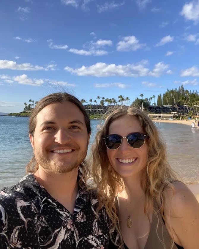 Ronny and a person posing for a selfie on a beach with the ocean, sand and palm trees 