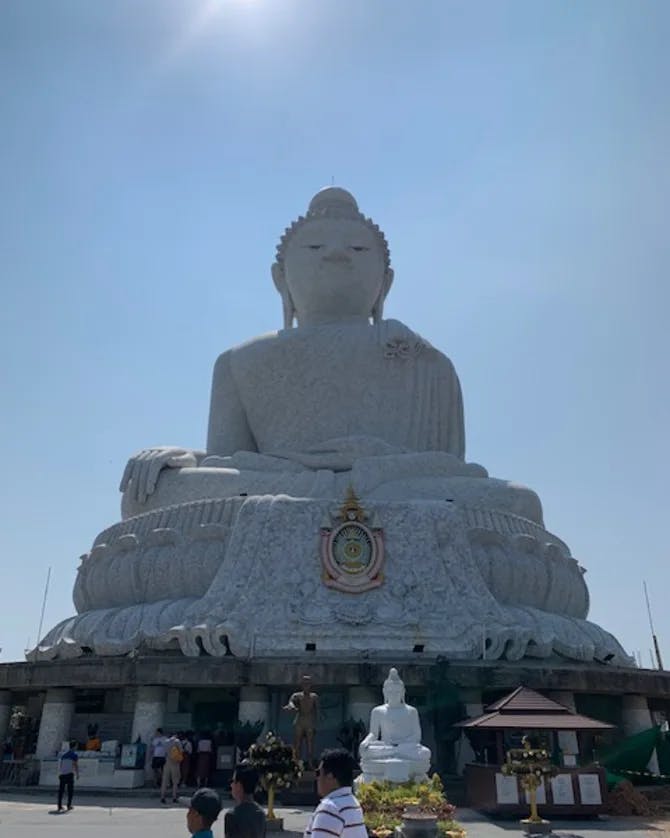 A large white statue of Buddha with clear skies and the sun shining. 