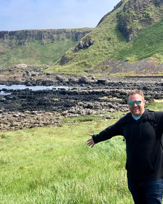 Travel advisor Michael in a black outfit standing at Giant's Causeway in a grassy meadow with hills in view