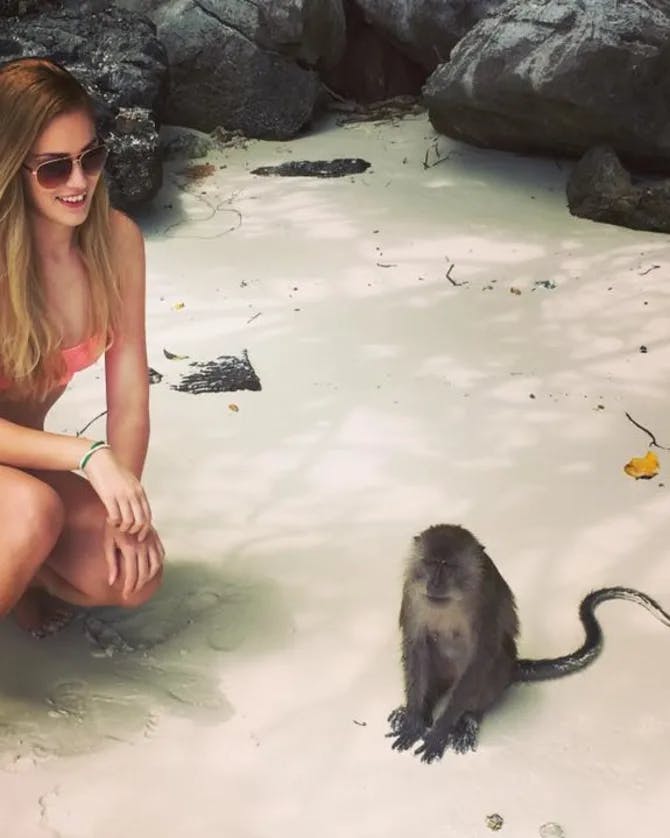 Girl posing with a monkey on sandy beach.