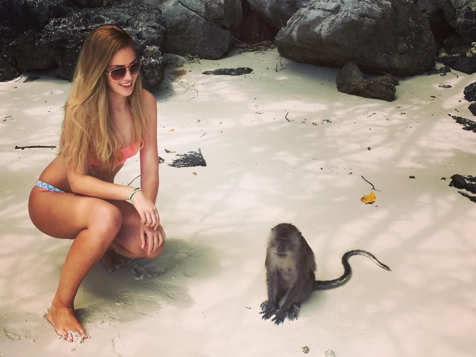 Girl posing with a monkey on sandy beach.