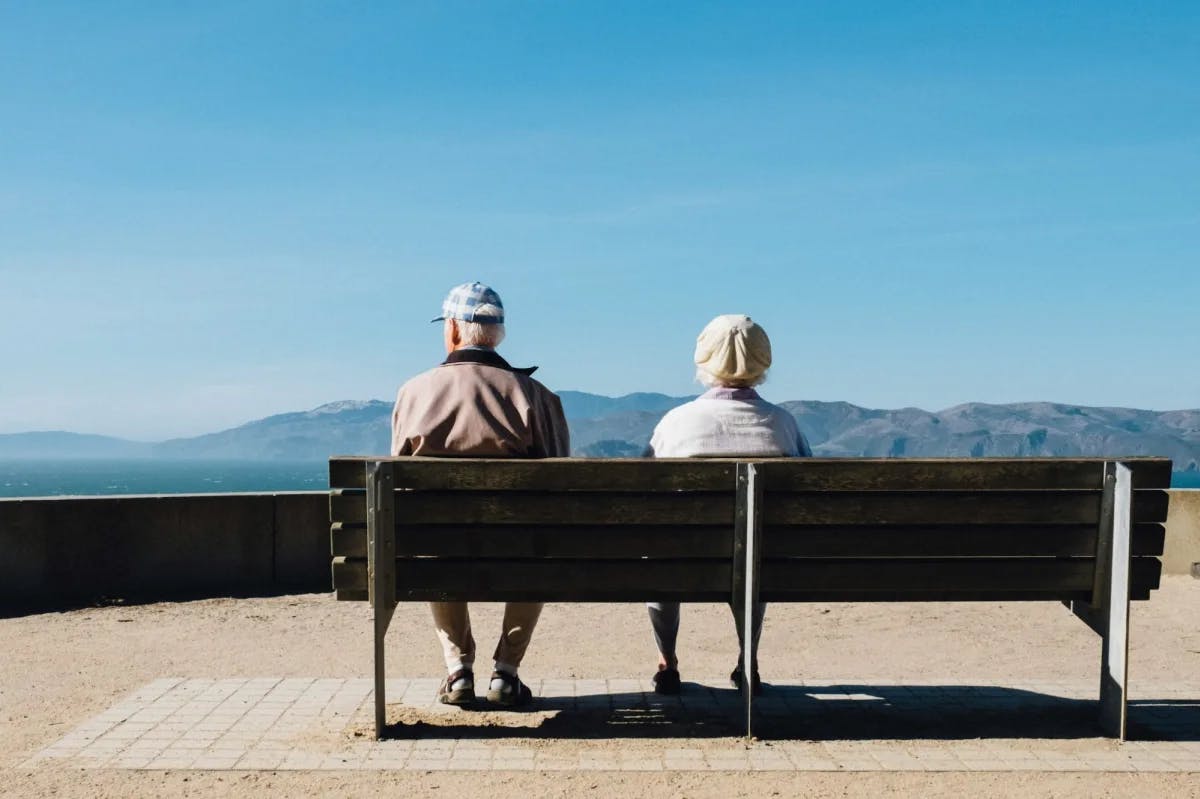 Backs turned to the camera while sitting on a wooden bench, an elder couple admires the view from Lands End in San Francisco