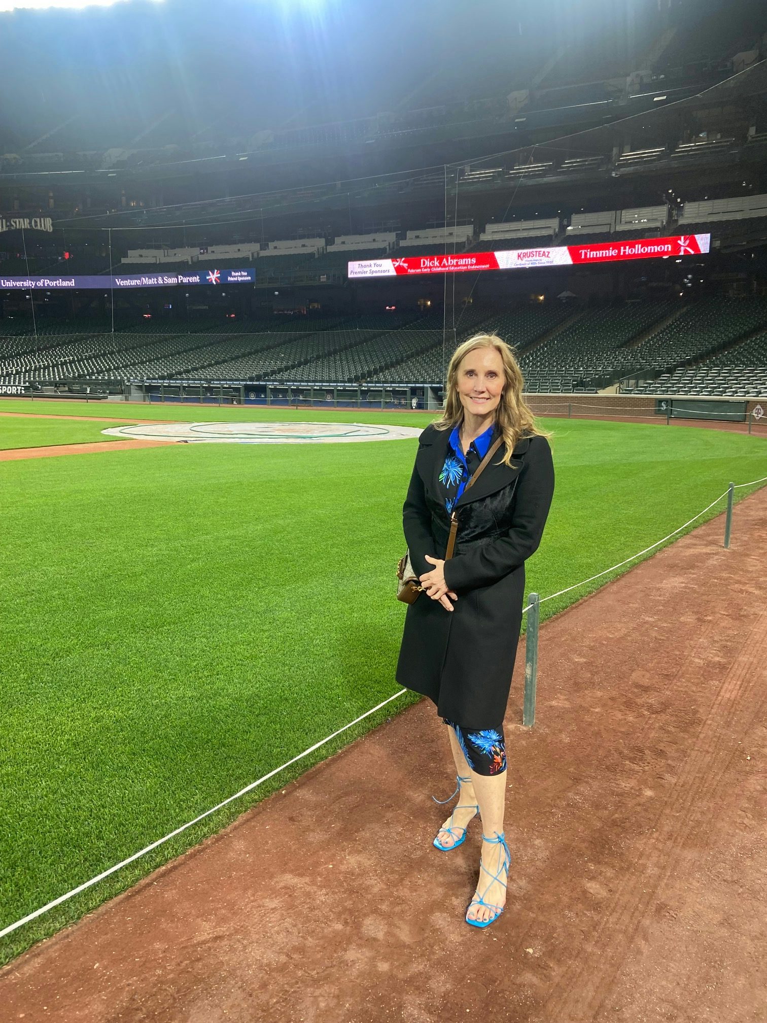Travel Advisor Regan Hurley wears a black suit and stands on an empty baseball stadium field 