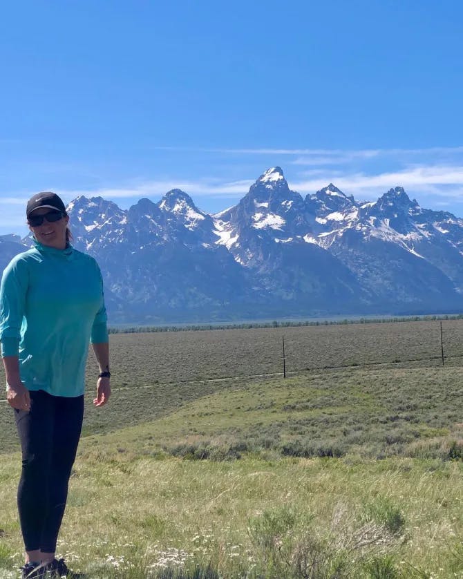 Katie wearing a blue jacket standing on grass in front of the mountains at Grand Teton National Park