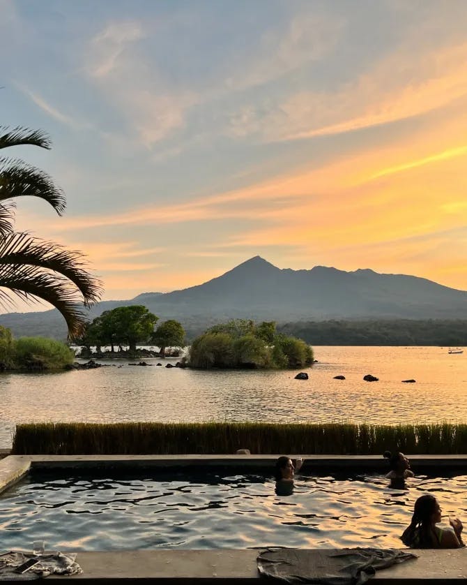 sunset over a tropical hotel pool with a mountain in the distance