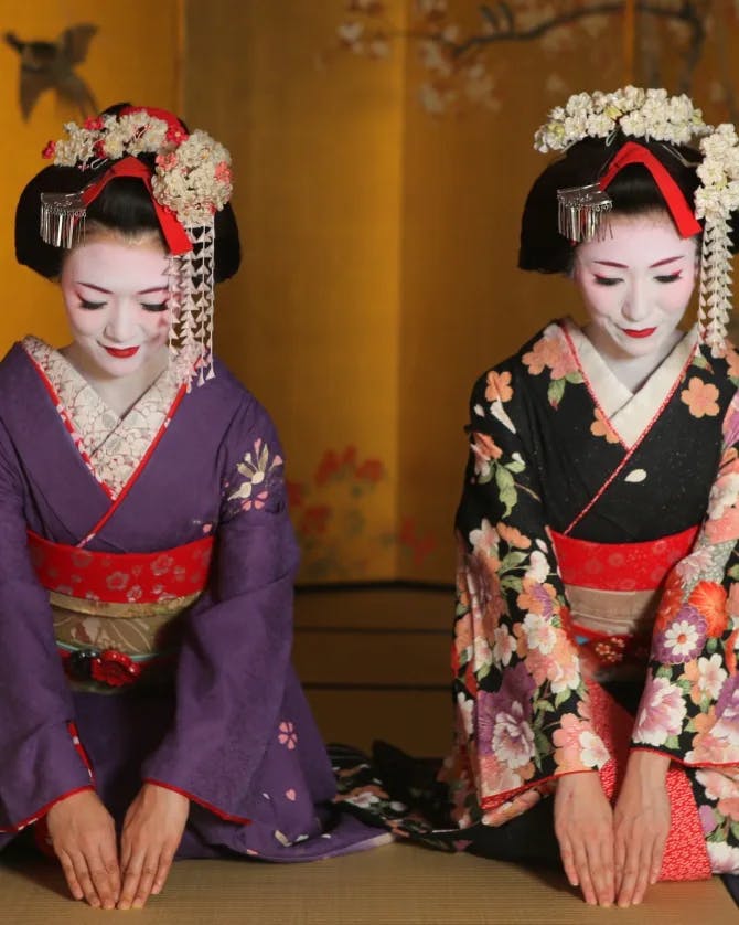 Two women dressed in Geisha apparel kneeling down.