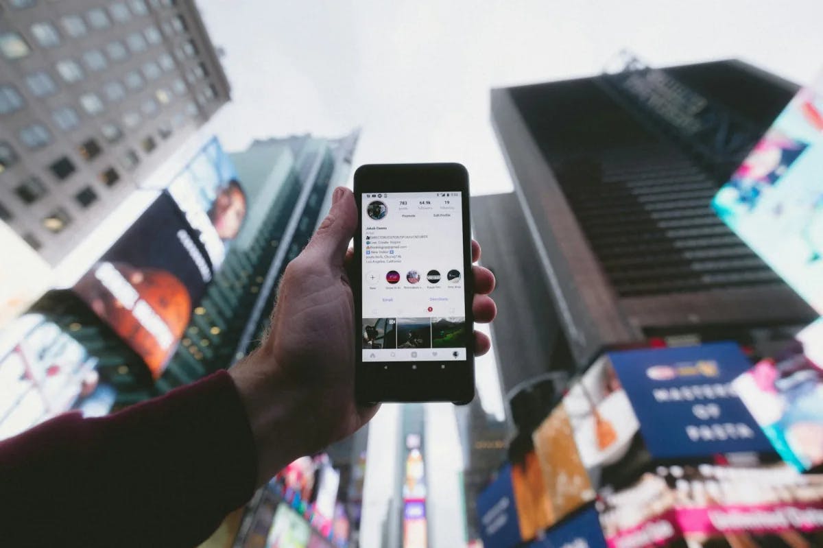 In Times Square, an unseen man holds his phone showing his Instagram profile before the skyline