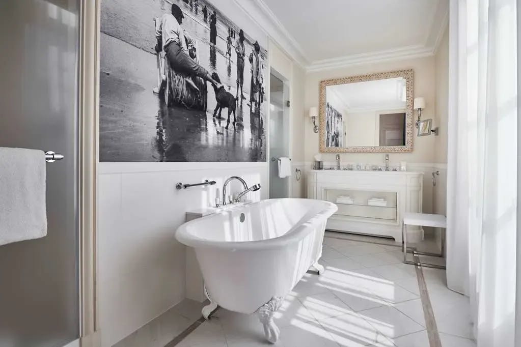 a white bathtub in a tiled bathroom with a black-and-white mural