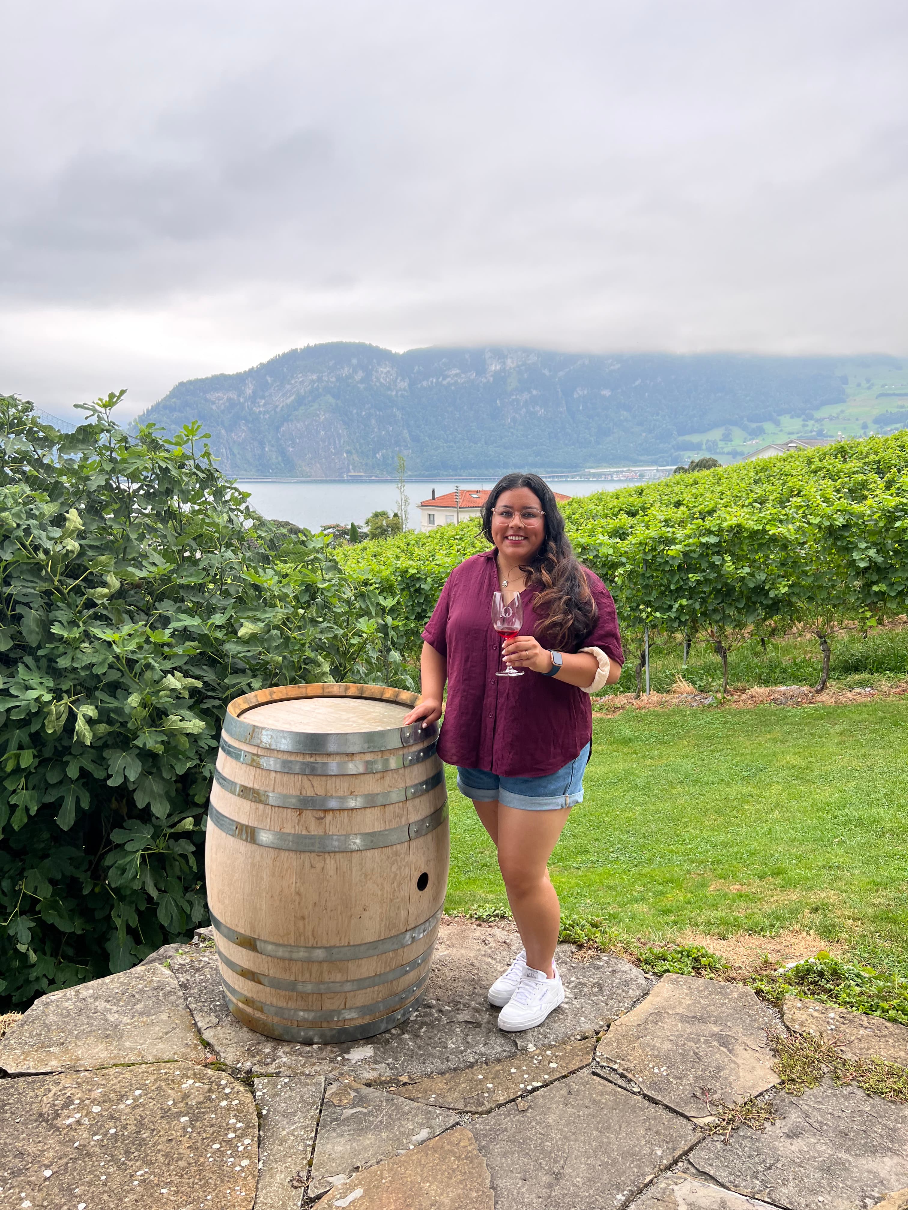 Pooja standing outside by a wine barrel, in a wine vineyard on an overcast day.