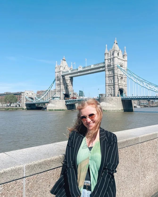 Picture of Merritt at Tower Bridge in London on a sunny day wearing a green top, black jacket and sunglasses