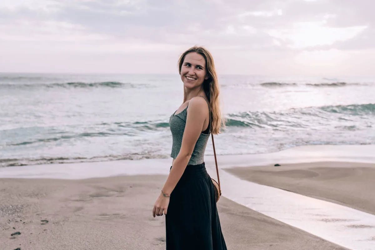 a woman in a tank-top and black pants stands on a beach