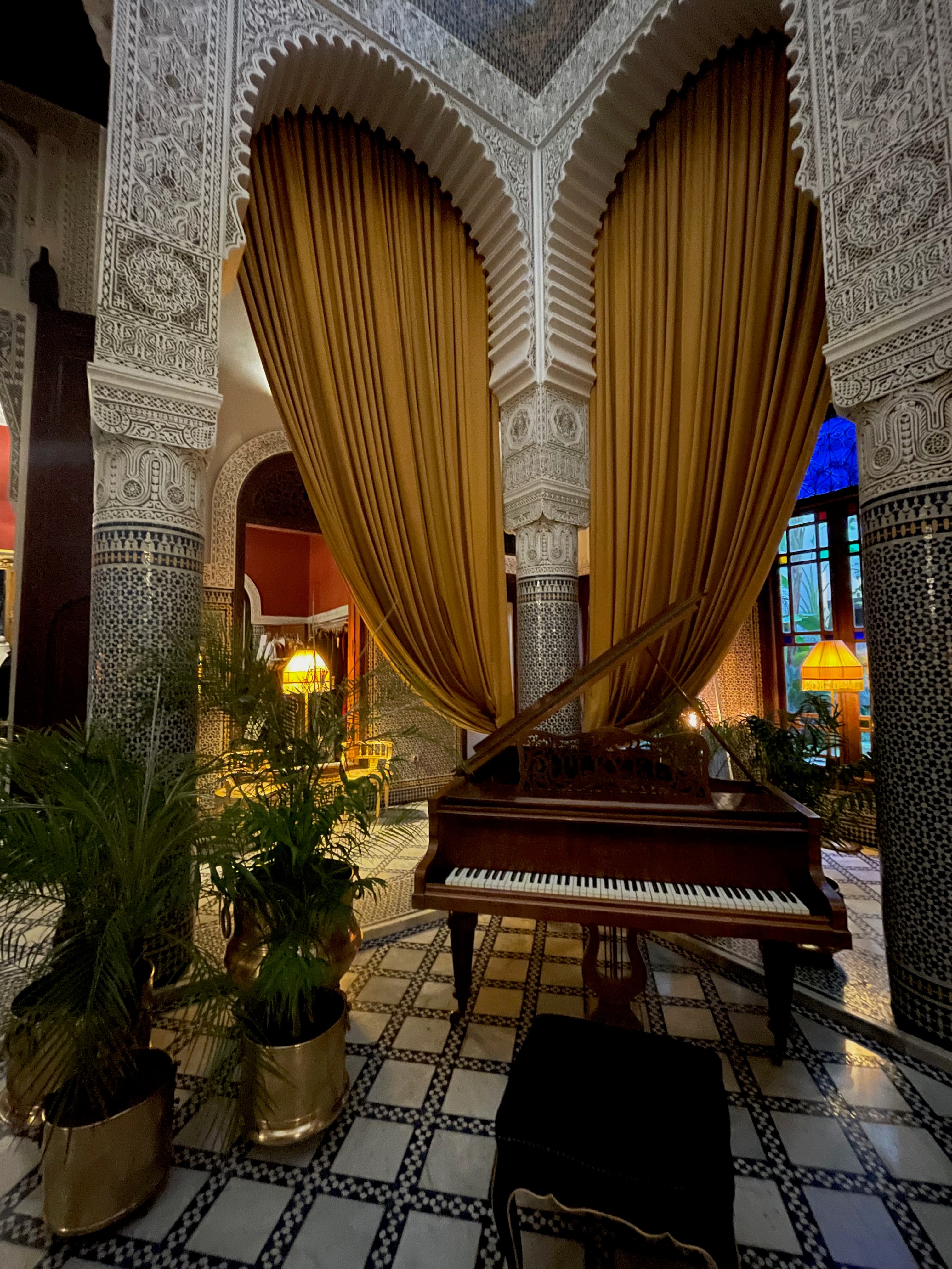 The lobby at the Riad Fes on day one of a Morocco 7 day itinerary, with a piano, marble columns and dramatic orange curtains.